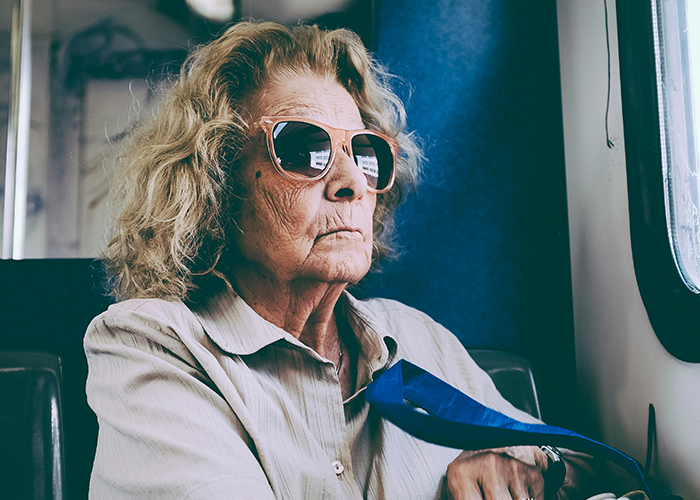 Elderly woman with sunglasses, sitting indoors, reflecting on son's girlfriend's house rule. Elderly woman with sunglasses, sitting indoors, reflecting on son's girlfriend's house rule.