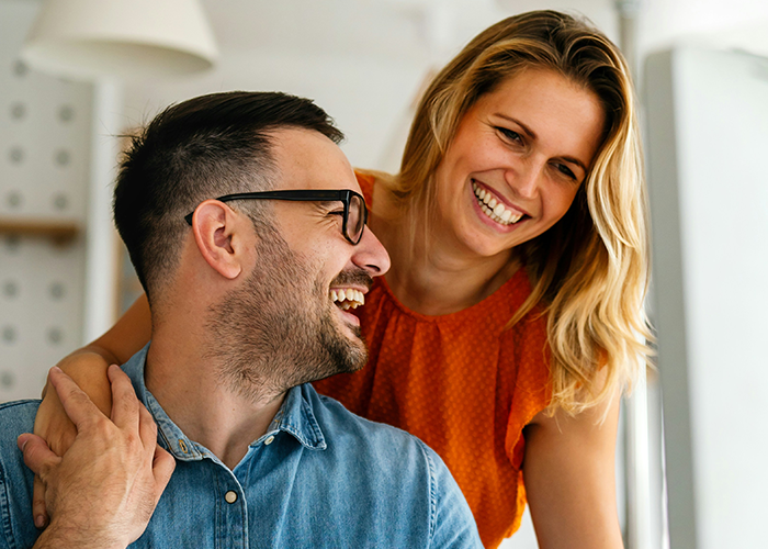 Man with smiling woman, representing work-wife scenario, both laughing indoors. Man with smiling woman, representing work-wife scenario, both laughing indoors.