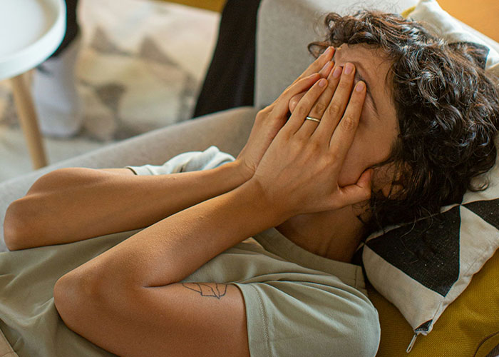 A woman feeling sad and overwhelmed, covering her face with her hands, lying on a sofa. A woman feeling sad and overwhelmed, covering her face with her hands, lying on a sofa.