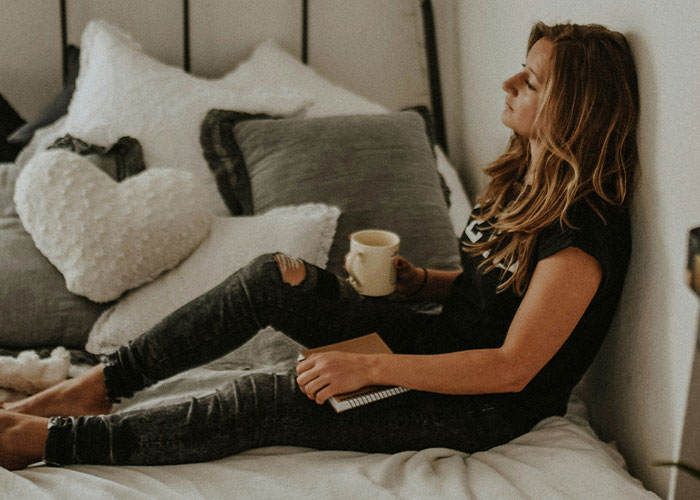 Woman sitting on bed with a mug, deep in thought, symbolizing emotional distance caused by an insidious work wife. Woman sitting on bed with a mug, deep in thought, symbolizing emotional distance caused by an insidious work wife.