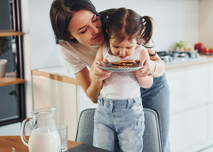 Mother and child in kitchen, practicing gentle parenting, holding a plate of cookies together. Mother and child in kitchen, practicing gentle parenting, holding a plate of cookies together.