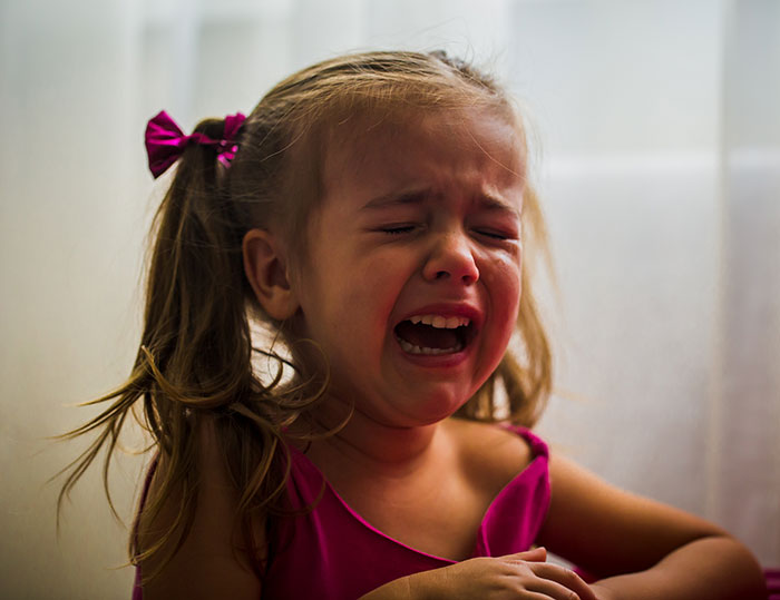Young girl in a pink dress crying, illustrating child inclusion issues at a spa event. Young girl in a pink dress crying, illustrating child inclusion issues at a spa event.