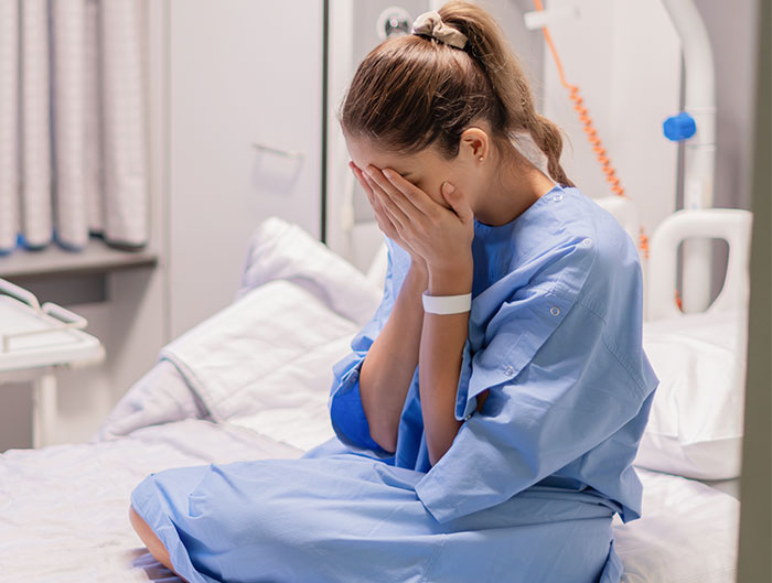 Woman in hospital gown sitting on bed, covering face, reflecting on adoption decision. Woman in hospital gown sitting on bed, covering face, reflecting on adoption decision.