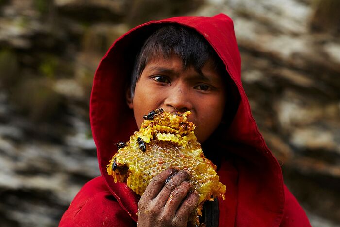 Child in a red hood eating honeycomb, showcasing global culture and tradition.