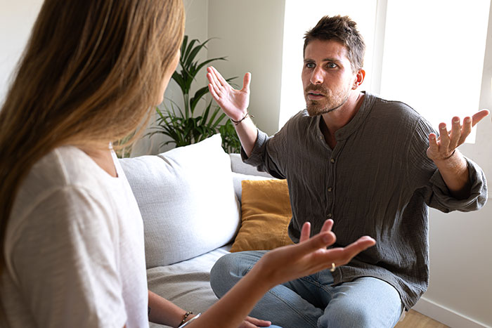 Man and woman discussing car bill payments, gesturing in a living room setting, related to sharing financial responsibilities. Man and woman discussing car bill payments, gesturing in a living room setting, related to sharing financial responsibilities.