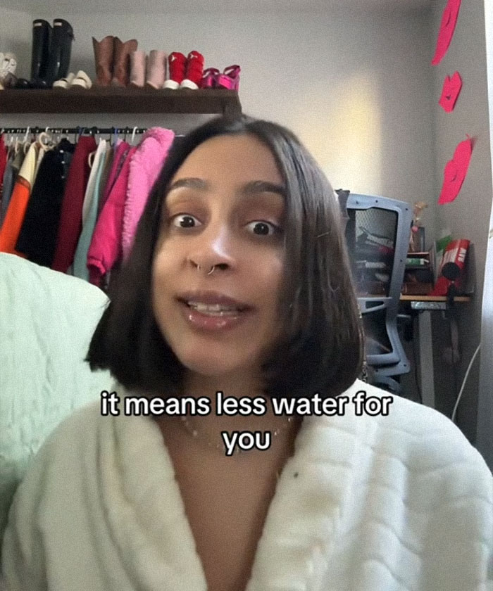 Woman discusses AI's environmental impact in a cozy room setting with clothing and shoes in the background. Woman discusses AI's environmental impact in a cozy room setting with clothing and shoes in the background.