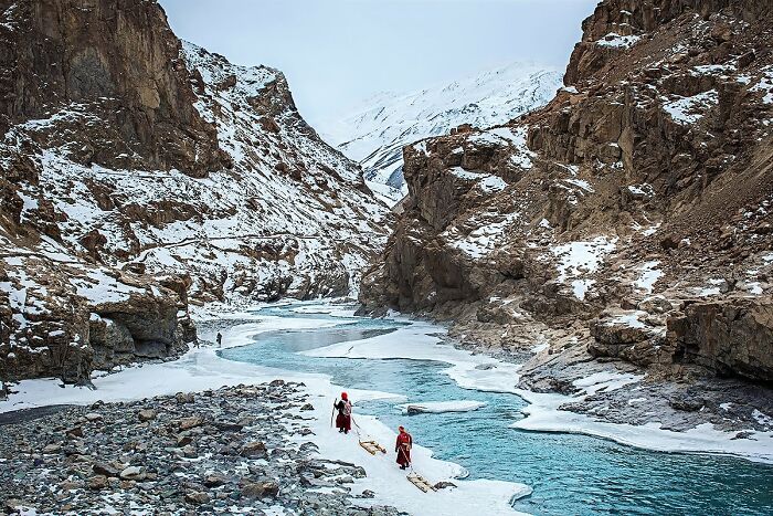 Travelers trekking on a frozen river surrounded by snow-covered mountains, showcasing global culture and tradition.