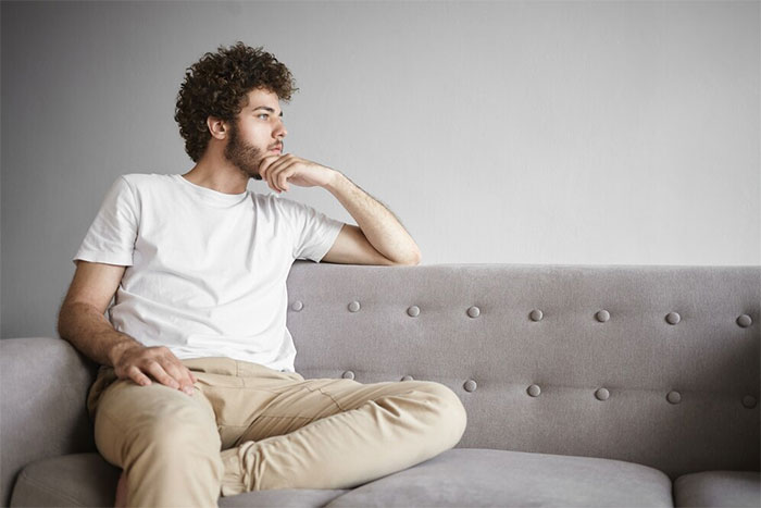 Man in casual wear sitting on gray sofa, reflecting on a dry wedding decision. Man in casual wear sitting on gray sofa, reflecting on a dry wedding decision.