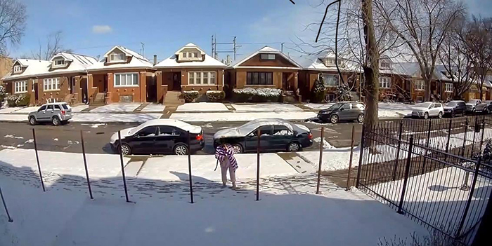 Woman on snowy street beside cars and houses. She appears to be examining or interacting with metal posts, possibly related to a fence. Woman on snowy street beside cars and houses. She appears to be examining or interacting with metal posts, possibly related to a fence.