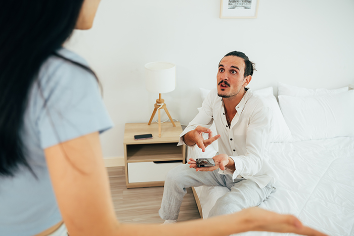 Man surprised about wife's secret monitoring, holding phone in bedroom discussion. Man surprised about wife's secret monitoring, holding phone in bedroom discussion.