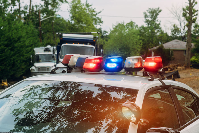 Police car with lights on in a suburban neighborhood, trees and houses visible in the background. Police car with lights on in a suburban neighborhood, trees and houses visible in the background.
