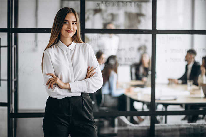 Confident woman in a white shirt standing in office, embodying malicious compliance in a modern workspace. Confident woman in a white shirt standing in office, embodying malicious compliance in a modern workspace.