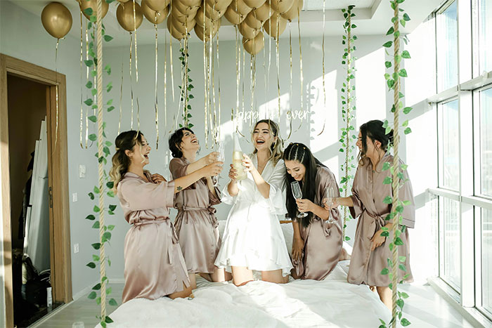 Women celebrating in a room with balloons, wearing robes, symbolizing bachelorette party festivities. Women celebrating in a room with balloons, wearing robes, symbolizing bachelorette party festivities.