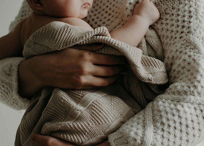 A person holding a baby wrapped in a knit blanket, symbolizing adoption and family decisions. A person holding a baby wrapped in a knit blanket, symbolizing adoption and family decisions.