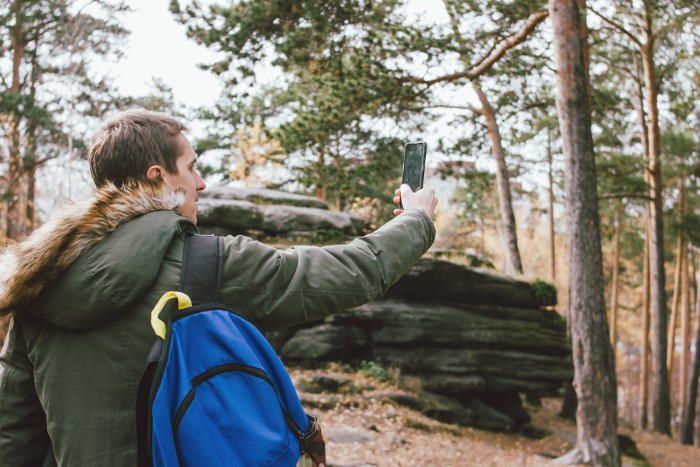 Man with a blue backpack taking a photo in a forest setting, relating to malicious compliance. Man with a blue backpack taking a photo in a forest setting, relating to malicious compliance.