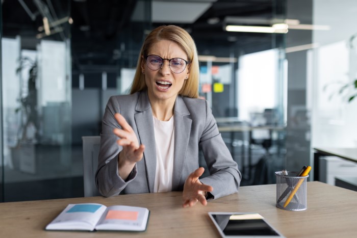 Woman in office gesturing emphatically, wearing a gray suit and glasses, representing an egoistic boss. Woman in office gesturing emphatically, wearing a gray suit and glasses, representing an egoistic boss.