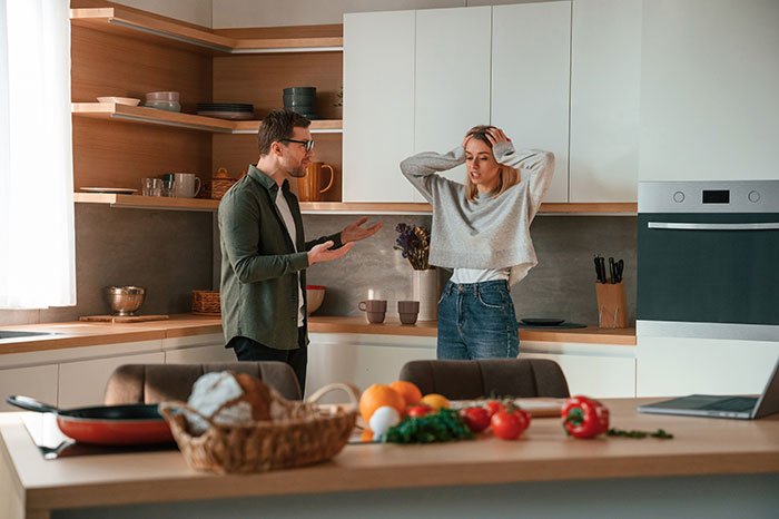 Man and woman in kitchen, discussing weaponized incompetence during an argument. Man and woman in kitchen, discussing weaponized incompetence during an argument.