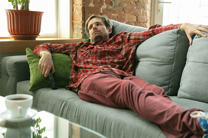 Man in plaid shirt lounging on a couch, representing concept of weaponized incompetence. Man in plaid shirt lounging on a couch, representing concept of weaponized incompetence.