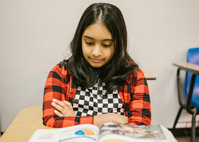 Girl sitting at a desk in a classroom, looking at a book, symbolizing a teacher pronouncing names incorrectly. Girl sitting at a desk in a classroom, looking at a book, symbolizing a teacher pronouncing names incorrectly.