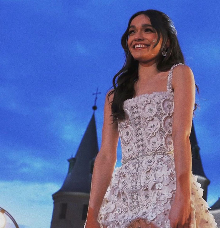 Young woman in a detailed white dress, smiling in front of castle-like towers at dusk, related to Snow White movie discussion. Young woman in a detailed white dress, smiling in front of castle-like towers at dusk, related to Snow White movie discussion.