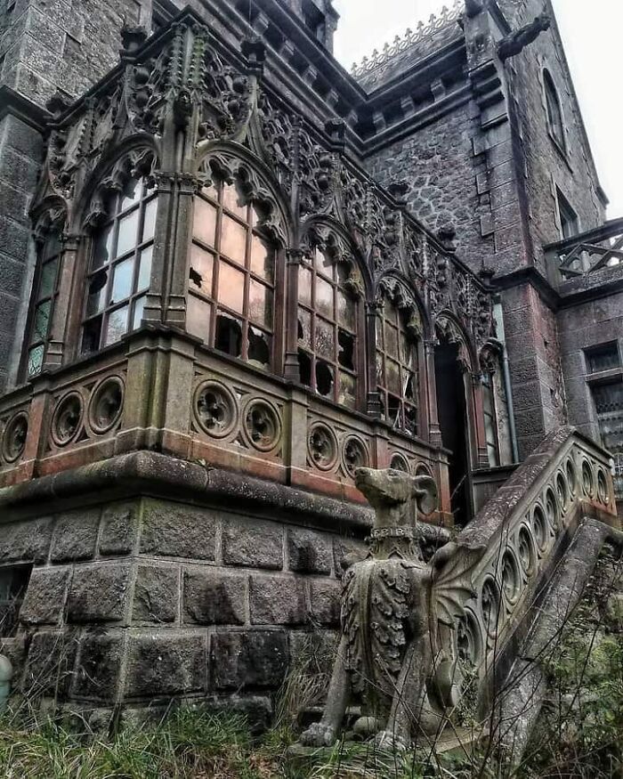 Abandoned place with ornate stone facade and broken windows, featuring statues and intricate designs.