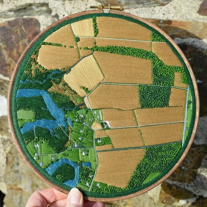Handcrafted landscape embroidery depicting fields and rivers in a circular hoop.