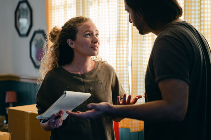 Man and woman discussing wedding issues, holding a notebook, with a tense expression in a home setting. Man and woman discussing wedding issues, holding a notebook, with a tense expression in a home setting.