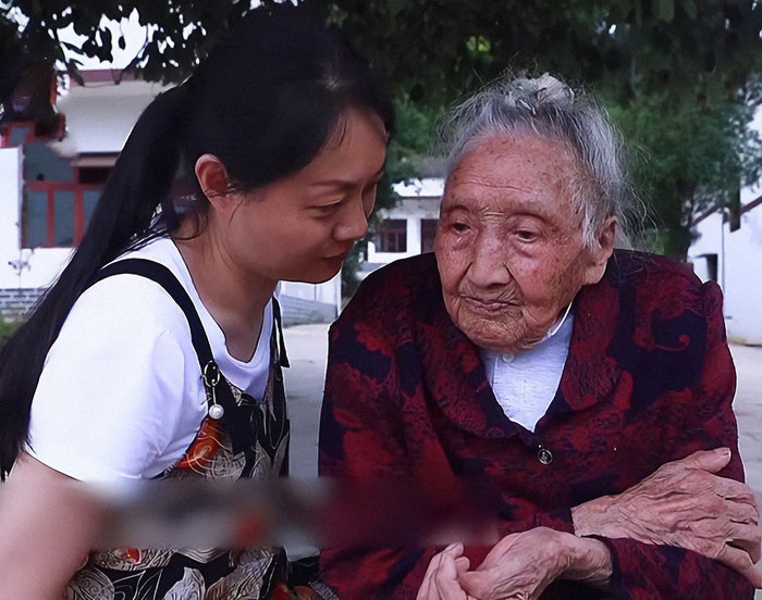 Elderly Chinese woman, 103, sitting outdoors with a young woman, wearing a red and black jacket, looking pensive. Elderly Chinese woman, 103, sitting outdoors with a young woman, wearing a red and black jacket, looking pensive.
