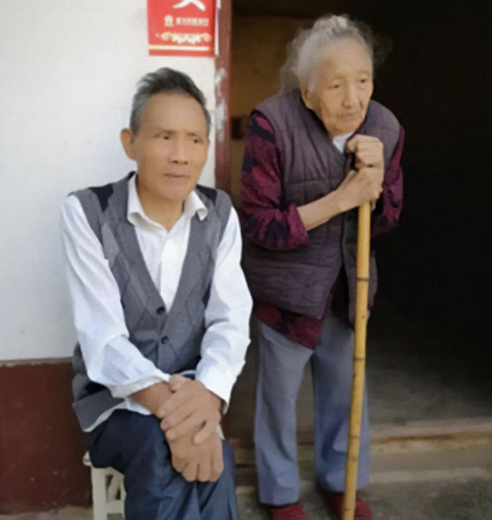 Elderly Chinese woman with a cane and man seated outside a home. Elderly Chinese woman with a cane and man seated outside a home.