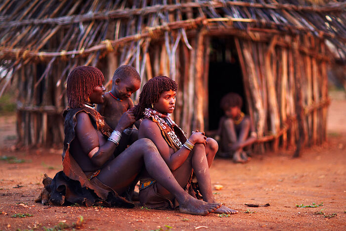 Women in traditional attire sitting outside a thatched hut, showcasing culture and tradition.