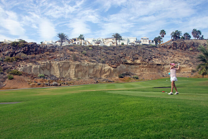 Golfer plays a round on a stunning course with scenic cliffs and homes in the background.