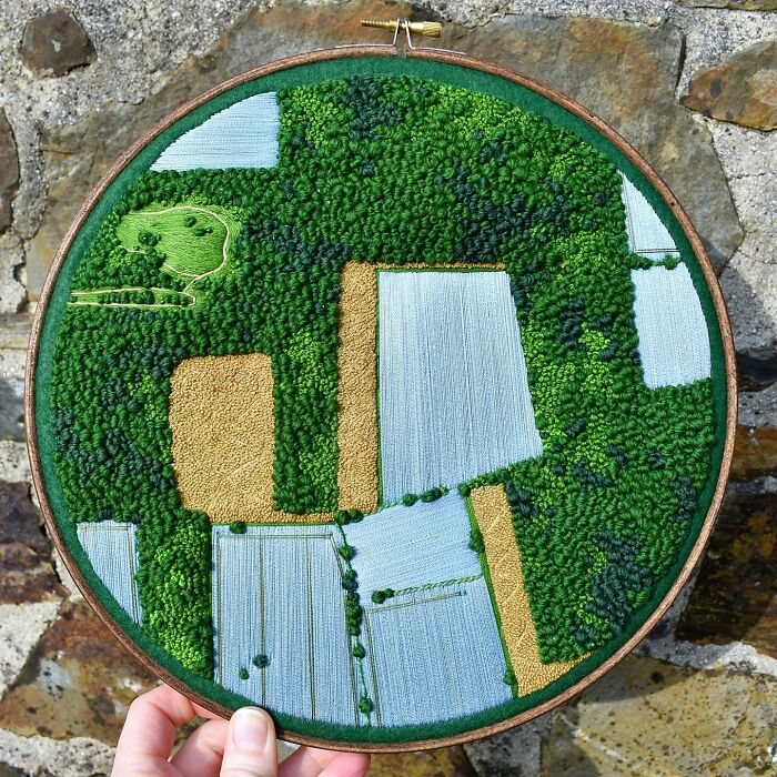 Landscape embroidery featuring lush fields and forests in a circular hoop, crafted with intricate detail.