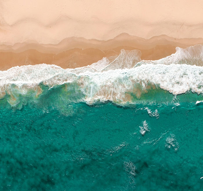 Aerial view of turquoise ocean waves crashing on sandy beach, demonstrating natural beauty and potential life-saving knowledge.