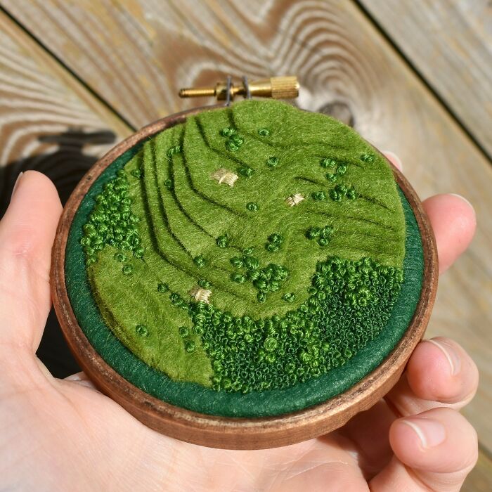 Landscape embroidery art held in a hand, showcasing textured green scenery.