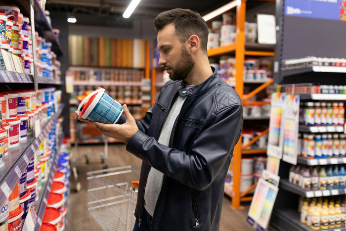 A man in a leather jacket holding a can in a store aisle, surrounded by colorful items. A man in a leather jacket holding a can in a store aisle, surrounded by colorful items.