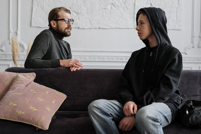 Man and teen talking on a couch, reflecting a parent-child interaction at home. Man and teen talking on a couch, reflecting a parent-child interaction at home.
