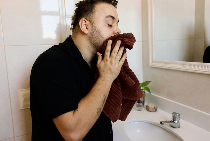 Man drying his face with a towel at the bathroom sink, illustrating everyday life-saving hygiene practices.