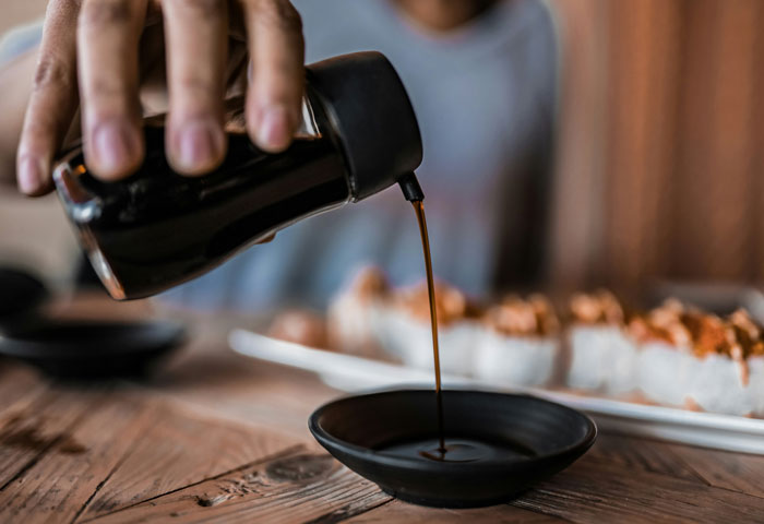 Pouring soy sauce into a dish near sushi, emphasizing careful food preparation.