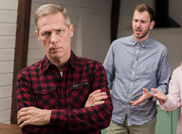 Father-in-law upset during a family discussion, with a man gesturing in the background. Father-in-law upset during a family discussion, with a man gesturing in the background.