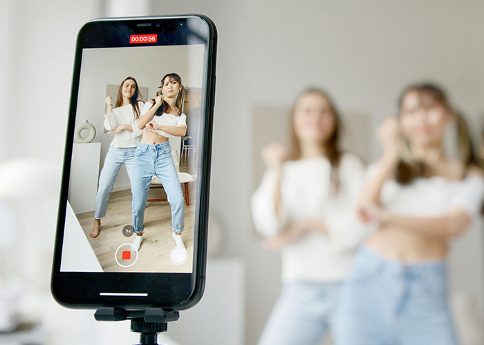 Influencers recording a video, both in white tops and jeans, highlighting fashion trends among influencers. Influencers recording a video, both in white tops and jeans, highlighting fashion trends among influencers.