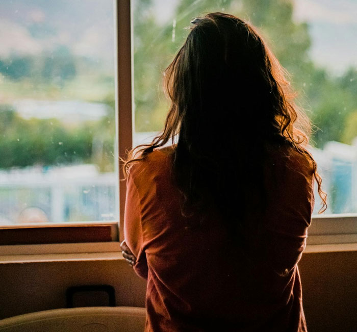 Woman looks out a window, contemplating in a dimly lit room, related to an ex-GF's cousin's relationship. Woman looks out a window, contemplating in a dimly lit room, related to an ex-GF's cousin's relationship.