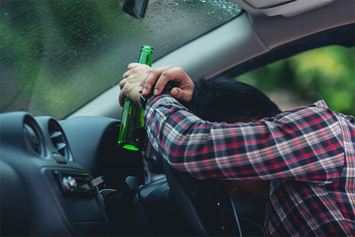 Man in car holding bottle, head on steering wheel, wearing plaid shirt, rainy window visible. Man in car holding bottle, head on steering wheel, wearing plaid shirt, rainy window visible.