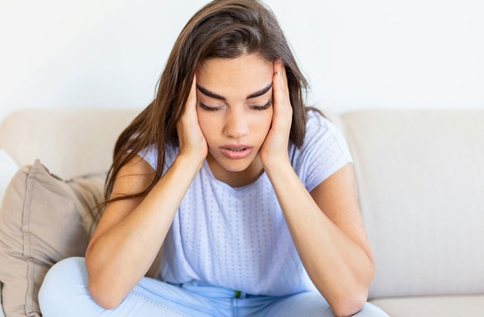 Stressed woman sitting on a couch, holding her head with both hands. Stressed woman sitting on a couch, holding her head with both hands.