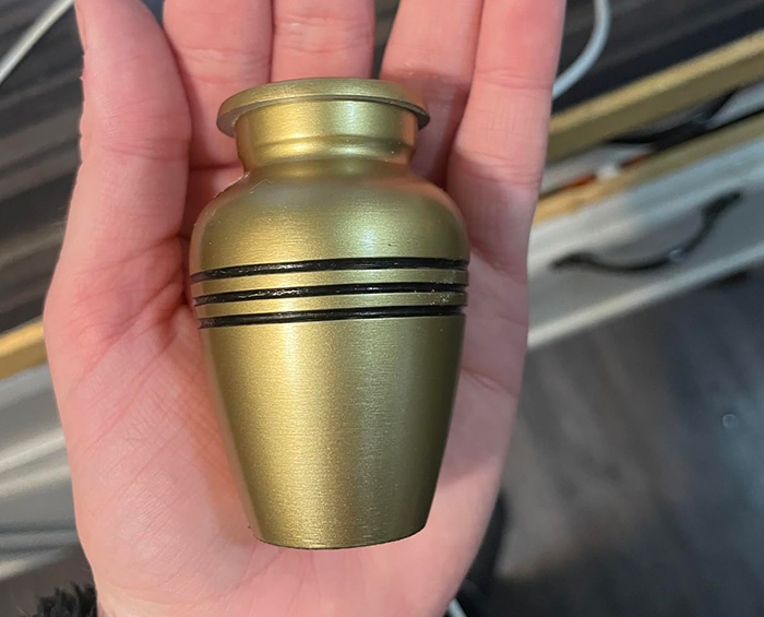 A small golden urn held in hand, symbolizing mourning a dog's ashes. A small golden urn held in hand, symbolizing mourning a dog's ashes.