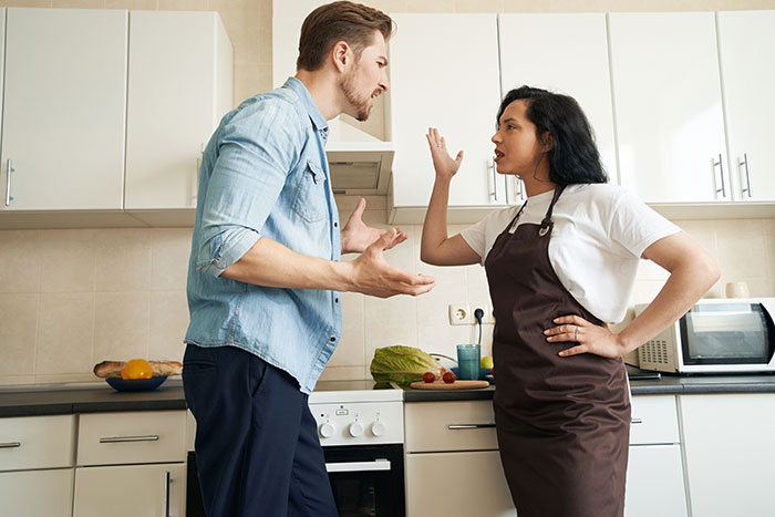 A couple arguing in a kitchen over a promotion, with vegetables on the counter. A couple arguing in a kitchen over a promotion, with vegetables on the counter.