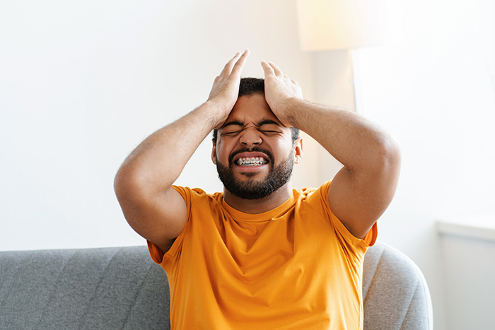 Man in an orange shirt on a sofa, expressing frustration and holding his head, conveying seething mad emotions. Man in an orange shirt on a sofa, expressing frustration and holding his head, conveying seething mad emotions.