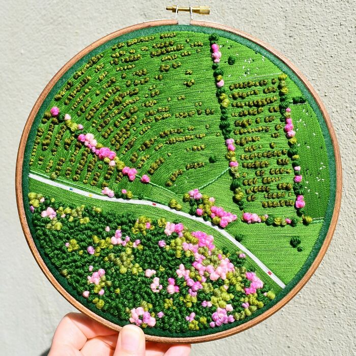 Handcrafted landscape embroidery featuring vibrant green fields and pink blossoms, showcasing intricate details and artistry.