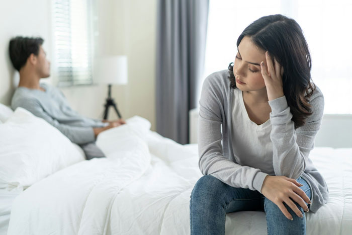 Couple experiencing tension, woman sitting upset on bed, reflecting sterilization decision against partner's wishes. Couple experiencing tension, woman sitting upset on bed, reflecting sterilization decision against partner's wishes.