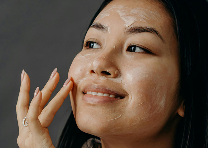 Woman applying cream on her face, demonstrating beauty tips for skincare routine.