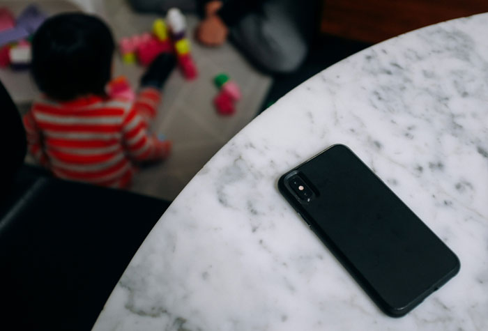 Child playing with blocks on floor, phone on a marble table in focus, reflecting a babysitting scenario for low pay discussion. Child playing with blocks on floor, phone on a marble table in focus, reflecting a babysitting scenario for low pay discussion.